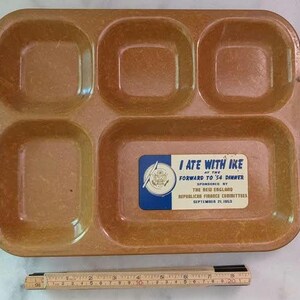 May include: A rectangular brown plastic divided tray with five compartments. A rectangular sticker reads: I ATE WITH IKE AT THE FORWARD TO '54 DINNER SPONSORED BY THE NEW ENGLAND REPUBLICAN FINANCE COMMITTEES SEPTEMBER 21, 1953. A ruler shows a length of 8 inches.