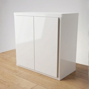 May include: A white, two-door cabinet with a glossy finish. The cabinet is rectangular and sits on a wooden floor. The doors are flush with the frame, creating a clean, modern look. The cabinet is a storage solution.