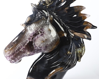 May include: A detailed sculpture of a horse's head, carved from a polished stone. The sculpture features a dark, glossy finish with areas of purple, brown, and white. The horse's open mouth reveals a cavity with a crystal-like interior.