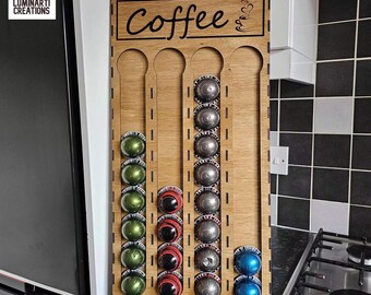 May include: Wooden coffee pod holder with the word "Coffee" engraved on the top. The holder has four columns with slots for coffee pods. The holder is made of light brown wood and has a natural wood finish.