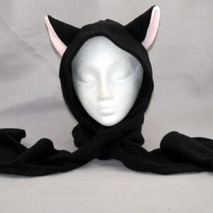 May include: Black fleece hooded scarf with pink cat ears. The scarf is tied around a white mannequin head.