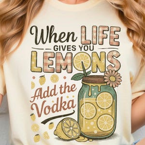 May include: Cream-colored t-shirt with the phrase "When Life Gives You Lemons, Add the Vodka" in a playful font. The design includes a mason jar filled with lemon slices and a daisy. A digital download.