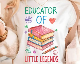Puede incluir: Camiseta blanca con el texto "EDUCATOR OF LITTLE LEGENDS" en verde, azul y rojo. El diseño incluye una pila de libros, un lápiz y varios garabatos coloridos. Artículo de descarga digital.