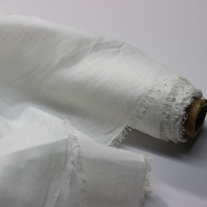 Pode incluir: Um rolo de tecido de linho branco com uma borda desfiada. O tecido é macio e tem uma textura natural.