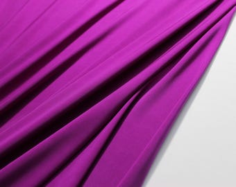 May include: A close-up of a smooth, vibrant purple fabric with soft folds and wrinkles. The fabric is draped over a white surface.