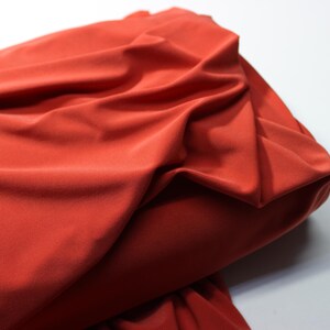 May include: A close-up of a rust-colored fabric with a smooth, silky texture. The fabric is folded and draped, showcasing its drape and flow.