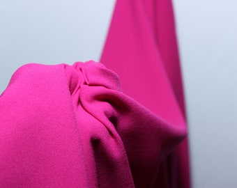 May include: Close-up of a bright pink fabric with a textured surface. The fabric is draped and folded, creating soft curves and folds.