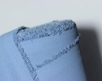 May include: Close-up of a light blue fabric with a frayed edge. The fabric is soft and textured.
