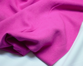 May include: A close-up of a bright pink fabric, showing its texture and folds. The fabric is soft and smooth, with a slight sheen.