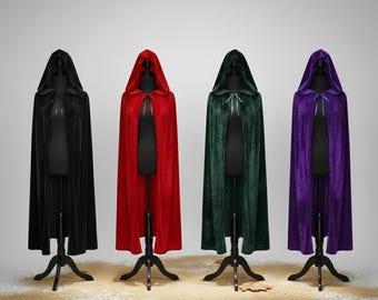 Op de afbeelding: Vier fluwelen capes met capuchon in zwart, rood, groen en paars, uitgestald op zwarte paspoppen. Elke cape heeft een capuchon en een striksluiting bij de hals. De capes staan op zwarte standaards.