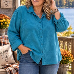 May include: A long-sleeved teal button-down shirt with a collared neckline and rolled cuffs, paired with blue denim jeans. The shirt features a textured fabric finish and a central row of matching teal buttons extending from the collar to the hem.