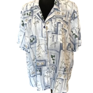 May include: A light blue short-sleeved button-up shirt with a floral print. The print features white flowers, green leaves, and gray geometric shapes.