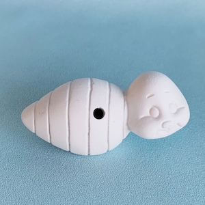 May include: White ceramic figurine shaped like a cocoon with a small hole in the side. The figurine has a textured surface and a rounded shape.