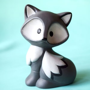 May include: A gray ceramic fox figurine with white accents and black detailing. The fox is sitting with its tail curled around its body.