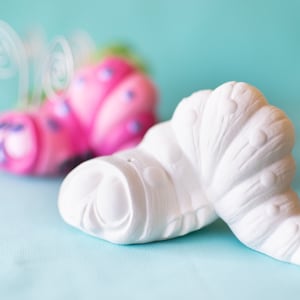 May include: A white ceramic seashell with a textured surface and a curled shape. The seashell is sitting on a light blue surface.