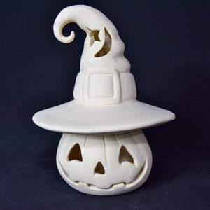 May include: White ceramic pumpkin with a witch's hat. The hat has a crescent moon cut-out and a curled brim. The pumpkin has a carved jack-o'-lantern face.