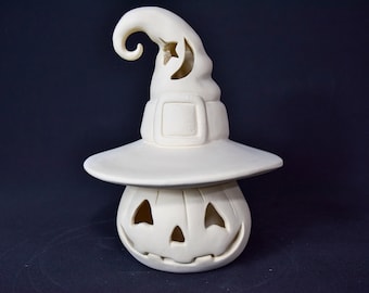 May include: White ceramic pumpkin with a witch's hat. The hat has a crescent moon cut-out and a curled brim. The pumpkin has a carved jack-o'-lantern face.