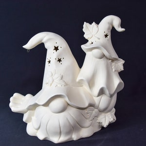 May include: White ceramic gnome figurine with a pointed hat and a leaf design. The gnome is sitting on a pumpkin with a smaller gnome figurine on top of it.