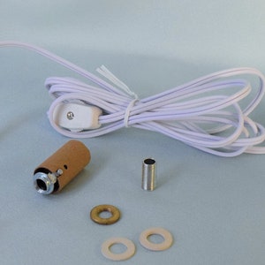 May include: A white electrical cord with a plug, inline switch, and a brown lamp socket. The cord is coiled and the socket is detached. There are also two white and one brass washers and a silver metal connector.