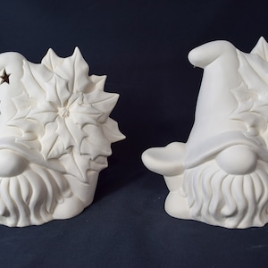 Puede incluir: Dos gnomos de cerámica blanca con diseños de poinsettia en sus sombreros. Los gnomos tienen barbas y están sentados sobre una base.