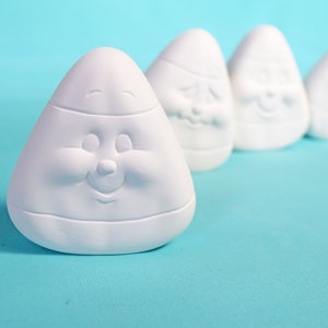 May include: Five white ceramic candy corn figurines with smiling faces. The candy corn are arranged in a row on a light blue background.