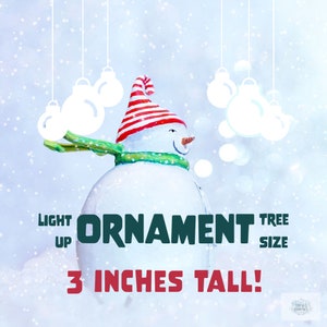 May include: A white snowman ornament with a red and white striped hat and a green scarf. The ornament is 3 inches tall and is a light up Christmas tree ornament.