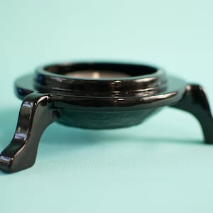 Pode incluir: Casti&ccedil;al de metal preto com tr&ecirc;s pernas e topo redondo. O casti&ccedil;al &eacute; projetado para segurar uma vela pequena.