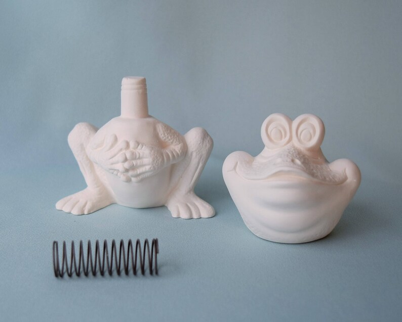 Pu&ograve; includere: Due statuine di rana in ceramica bianca. Una rana &egrave; seduta con le gambe distese e ha un buco nella parte superiore della testa. L'altra rana &egrave; sdraiata a bocca aperta.