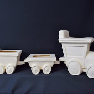 May include: White ceramic train engine and two boxcars. The engine has a whistle and a bell. The boxcars have open tops. The train is a planter.