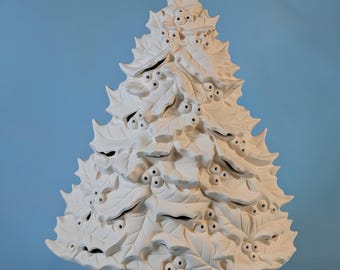Puede incluir: Un árbol de Navidad de cerámica blanca con un diseño de hojas y bayas de acebo. El árbol está sobre una base redonda con detalles de hojas de acebo. El árbol no está pintado y está listo para personalizar.