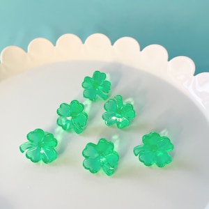 May include: Six green four-leaf clover charms on a white plate with a scalloped edge.