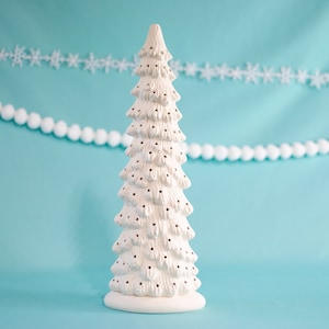 May include: White ceramic Christmas tree with a textured surface and holes for lights. The tree is on a light blue background.