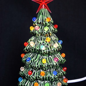 May include: A ceramic Christmas tree with a red star on top and multi-colored lights. The tree is green and has a textured surface.