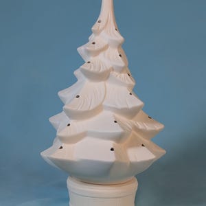 May include: A white ceramic Christmas tree with a textured surface and small holes for lights. The tree has a conical shape with layered branches and sits on a round base. The background is a solid blue.