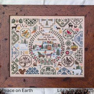 May include: A framed cross-stitch sampler with a winter village scene and the text "Peace on Earth Goodwill to men." The sampler is surrounded by a variety of smaller designs, including animals, birds, and flowers. The frame is a dark brown wood.