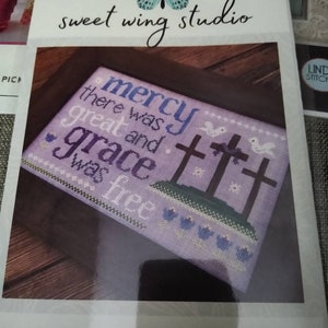 May include: Cross stitch pattern featuring a purple background with the text "mercy there was great and grace was free" and two crosses. The pattern is titled "mercy & grace".