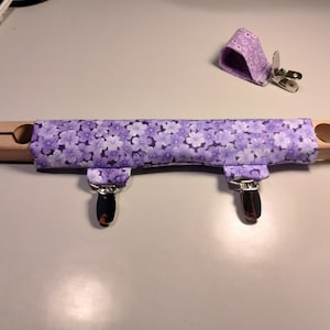 May include: A purple and white floral fabric covered wooden sewing tool with two metal clips.