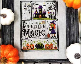 May include: A framed counted cross stitch pattern with a Halloween theme. The design features a haunted house, witch, pumpkins, and the words "Make a Little Magic." The frame is surrounded by orange and white pumpkins.
