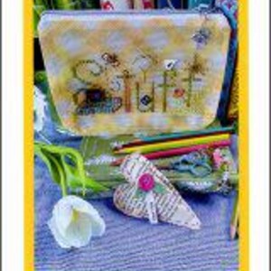 May include: A small, yellow and white patterned mini bag with the text "Stuff" embroidered on the front. The bag is open, revealing pencils, scissors, and other craft supplies. A white tulip and a heart-shaped item are in the foreground.
