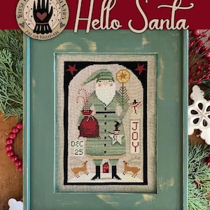 May include: A framed cross-stitch featuring Santa Claus in a green outfit, holding a bag and a tree. The text "Hello Santa" is above the image. The word "JOY" is vertically displayed. The date "DEC 25" is also visible. The frame is green.