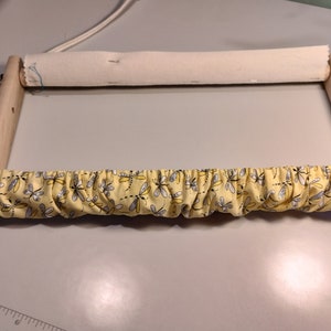 May include: A wooden embroidery hoop with a white fabric stretched across the top and a yellow fabric with a dragonfly pattern stretched across the bottom.