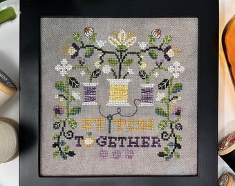 May include: A cross-stitch embroidery design featuring three spools of thread with flowers and vines surrounding them. The text "Stitch Together" is embroidered below the spools.