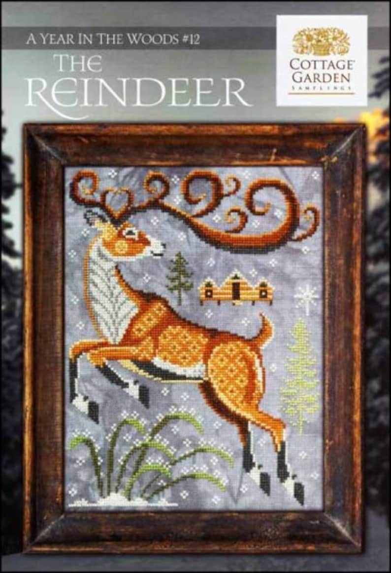 May include: A cross-stitch pattern featuring a reindeer with antlers, a snowy landscape, and a small cabin. The pattern is titled "The Reindeer" and is part of the "A Year in the Woods" series. The pattern is from Cottage Garden Samplings.
