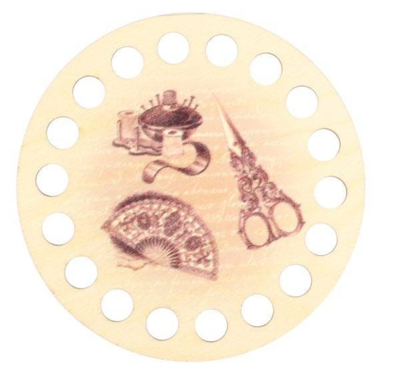 Pu&ograve; includere: Un portarotolo di filo rotondo in legno con un disegno color seppia con strumenti di cucito: forbici, un cuscinetto per spilli e un ventaglio. Il supporto ha pi&ugrave; fori circolari attorno al bordo.