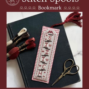 May include: A bookmark with the words "Stitch Spools" embroidered in red and black thread. The bookmark is on top of a dark book, with embroidery floss and small scissors nearby. The bookmark has a red tassel and a gingham border. The image also includes the text "Counted Cross Stitch Pattern by Textilly™ Copyright 2025."