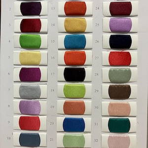 May include: A color swatch chart featuring 33 fabric samples in various colors. The samples are rectangular with rounded ends, each mounted on a white card. Colors include red, purple, green, yellow, and blue.