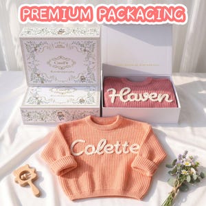 Premium gift packaging for CasaFit personalized baby sweaters, featuring custom hand-embroidered names on chunky knitwear inside elegant floral-themed gift boxes.