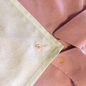 Op de afbeelding: Een roze overhemd met een witte kraag en een enkele knoop. Het overhemd heeft een monogram "KG" op de kraag.