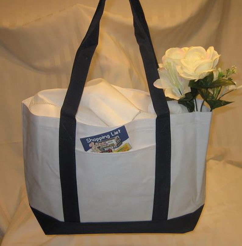 Puede incluir: Bolsa de lona blanca con asas y ribetes azul marino. La bolsa tiene un bolsillo grande en la parte delantera con una peque&ntilde;a tarjeta que dice "Shopping List" en su interior.