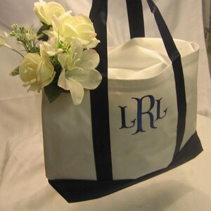 Puede incluir: Bolsa de lona blanca con asas negras e iniciales bordadas en azul "LRL". La bolsa est&aacute; decorada con un ramo de flores blancas.